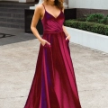 A woman stands outside in front of a building with steps and greenery, wearing a vibrant magenta and purple satin gown with a deep V-neckline and spaghetti straps. She has her hands in the dress pockets and is looking forward with a pleasant expression, embodying elegance from MONROE PO891. Angels Formal Wear