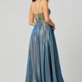 A woman stands gracefully wearing a flowing, metallic blue and green gown. The designer bridesmaid dress features a fitted bodice with intricate lace-up detailing on the back and thin straps. The skirt is long and slightly flared, shimmering with a textured, iridescent finish. Angels Formal Wear