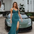 A woman in a teal evening gown with a thigh-high slit stands confidently in front of a green Lamborghini parked before an elegant white mansion with columns, perfectly capturing the luxurious vibe of the Sunshine Coast. She has one hand resting on her hip and the other on the car. Angels Formal Wear