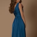 Woman with long, wavy brown hair wearing the NBM1002, a sleeveless, floor-length blue dress. She is standing sideways and looking over her shoulder against a plain brown background, exuding the effortless elegance reminiscent of the serene Sunshine Coast. Angels Formal Wear