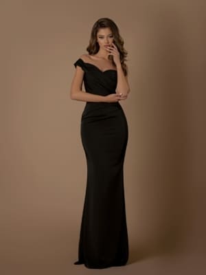 A woman with long wavy hair stands against a plain taupe background, showcasing the elegant off-the-shoulder, form-fitting black gown, NBM1019. She has one hand partially covering her mouth, giving a thoughtful expression, while her other arm is relaxed by her side. This dress is ideal for Sunshine Coast evenings and is available with Afterpay. Angels Formal Wear