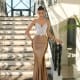 A woman stands on a grand staircase adorned with ornate black railings, wearing the ALITZA NC1018 evening gown from a Dress Shop on Sunshine Coast. The fitted, two-tone dress features a white lace bodice and a gold satin skirt. She strikes an elegant pose with her hand resting on the rail, surrounded by large windows and abundant natural light. Angels Formal Wear