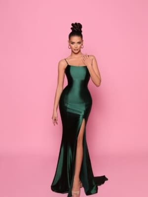 A woman stands against a pink backdrop, donning Sunshine Coast's Best Dress Shop's NP144 Deep—a sleek, dark green gown with thin straps and a thigh-high slit. Her hair is styled in an elegant updo, complemented by hoop earrings and high heels. She poses with one hand gently touching her face while the other rests at her side, capturing the essence of sophistication and elegance. Angels Formal Wear