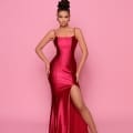 A woman poses confidently against a pink background, wearing the NP144 Deep, a form-fitting, sleeveless red gown with a high slit on one side. With an elegant updo hairstyle and subtle makeup, she completes her sophisticated look—perfectly showcasing the style from the Best Dress Shop on Sunshine Coast. Angels Formal Wear