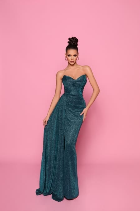 A woman wearing the elegant IZY NP149 teal strapless floor-length gown poses against a pink background. Her hair is styled in an updo, and she accessorizes with hoop earrings. The vibrant setting echoes the sunny vibes of Queensland’s Sunshine Coast. Angels Formal Wear