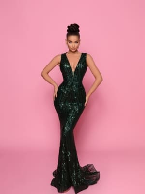 A woman stands against a pink background wearing the NP152, a form-fitting, sleeveless dark green dress adorned with sequin detailing and featuring a plunging neckline. Her hair is styled in an elegant updo as she confidently poses with her hands on her hips, capturing the vibrant essence of Queensland's Sunshine Coast. Angels Formal Wear