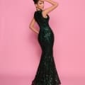 A woman graces a pink background in the NP152, an elegant, form-fitting dark green sequined gown featuring a fishtail design. Her hair is styled in an updo, and her right hand gracefully touches her head, accentuating her confident and glamorous look reminiscent of Sunshine Coast glamour in Queensland. Angels Formal Wear