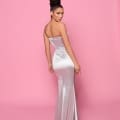 A woman in an elegant, strapless RITA NP165 silver gown from the Best Sunshine Coast Dress Shop poses against a pink background. Her hair is styled in a sleek updo, and she turns slightly to the side with one hand near her hip, showcasing the gown's fitted silhouette and floor-length design. Angels Formal Wear