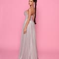 A woman stands against a pink background, wearing the LEXI NP176, a strapless shimmering gray gown flowing to the floor. Her long hair is styled in a sleek, high braid and she accessorizes with large hoop earrings. She faces slightly to the side, showcasing the gown's cocktail dress silhouette perfect for any Sunshine Coast event. Angels Formal Wear