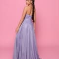 A woman with a long braided ponytail stands against a pink background, glancing over her shoulder. She is wearing the elegant LEXI NP176—a strapless, shimmering lavender gown that flows to the floor. Angels Formal Wear