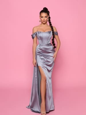 Against a pink background, a woman elegantly dons the NP185—a striking, off-the-shoulder silver gown featuring a thigh-high slit that makes it perfect for Sunshine Coast events. Her long braided hair cascades down as she accessorizes with large earrings and high-heeled sandals, creating an ideal ensemble for Race Day. Angels Formal Wear