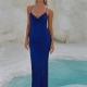 A person stands in front of an icy backdrop, wearing a long, royal blue evening wear dress with thin straps. They have light brown hair, styled straight and sleek. The scene includes bright turquoise water surrounded by white, textured terrain. Perfect for browsing ARA PO2438 at Dress Shop Sunshine Coast. Angels Formal Wear