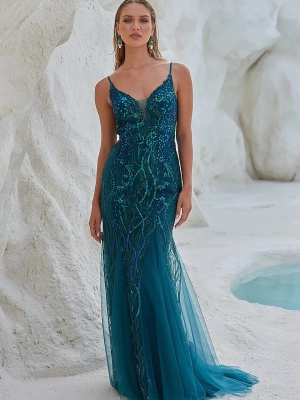 A woman stands against a textured, white rocky background, wearing a teal, sleeveless, floor-length gown adorned with intricate beadwork. Her long hair is styled loosely, and she wears matching teal earrings from OCEANE PO2461. A small pool of water is visible in the background. Angels Formal Wear