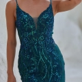 A woman poses in a fitted, teal-colored dress adorned with sparkling blue and green sequins and intricate beadwork. The OCEANE PO2461, available from Online Formal Wear Australia, has thin straps and a plunging neckline with a sheer inset. She rests one hand on her head, her long hair cascading over her shoulders. Angels Formal Wear