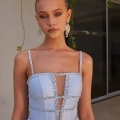 A woman stands in front of a building with plants hanging behind her. She is wearing a light blue sparkly dress with thin straps and intricate beading around the neckline and waist called GUINEVERE PO2473 from an Online Dress Shop in Australia. She has her hair pulled back and is wearing long, dangling earrings. Angels Formal Wear