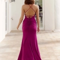 A woman with shoulder-length hair is walking away, wearing a floor-length, backless fuchsia dress with crisscross straps and a ruched design from AMELIA PO999. She is in an elegant setting with tall windows and vintage-style lanterns mounted on the wall. Angels Formal Wear