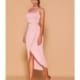 A woman stands against a light brown background, dazzling in a light pink, one-shoulder, sleeveless dress from BIANCA LD1125. The dress features an asymmetrical hemline and a high slit. She complements her chic look with strappy high-heeled sandals and an elegant updo. Angels Formal Wear