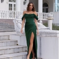 A woman wearing an off-the-shoulder, emerald green gown from CARMI PO979, with a thigh-high slit, stands on an outdoor staircase. She has shoulder-length hair and is posing in front of a white building with classical architectural elements like columns and arched windows. Angels Formal Wear