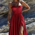 A woman wearing the stunning DAPHNE PO927 with a sweetheart neckline and high slit stands outdoors against a rocky background. She has shoulder-length hair and is accessorized with elegant earrings. Angels Formal Wear