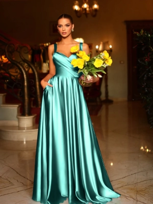 A woman in an elegant teal satin gown stands in a sophisticated indoor setting, reminiscent of EMMY BB210 on Sunshine Coast. She holds a bouquet of yellow flowers in one hand and has the other hand in her dress pocket. The background features a grand staircase and ornate decor. Angels Formal Wear