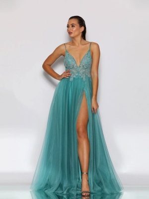 A woman stands confidently in a long, teal gown with a deep V-neckline and intricate embellishments on the bodice. The HARMONY JX2099, available at Dress Shop Sunshine Coast, features a high slit revealing one leg. She has her hair pulled back and is posing against a plain white background. Angels Formal Wear