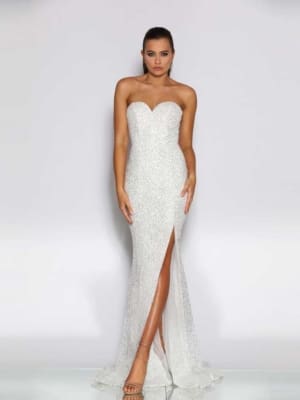 A person is standing against a plain background, wearing a strapless, fitted white gown with a sweetheart neckline and a thigh-high slit. The JASMINA JX2011, perfect for formal wear, is embellished with sequins, and the person is wearing strappy high-heeled sandals. Find exquisite styles like this at Dress Shop Sunshine Coast. Angels Formal Wear