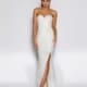 A person is standing against a plain background, wearing a strapless, fitted white gown with a sweetheart neckline and a thigh-high slit. The JASMINA JX2011, perfect for formal wear, is embellished with sequins, and the person is wearing strappy high-heeled sandals. Find exquisite styles like this at Dress Shop Sunshine Coast. Angels Formal Wear