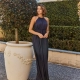 A woman in a long, sleeveless, dark blue dress stands next to a large decorative LINDEN TO880 with a small tree. She is in an outdoor setting on the Sunshine Coast, with neatly trimmed hedges and a beige building with white-trimmed windows in the background. Angels Formal Wear