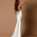 A woman stands on a neutral backdrop, modeling a floor-length, backless ivory gown. This stunning piece of formal wear features a mermaid silhouette with a flowing train. She poses with one arm raised gracefully to her forehead and her long, wavy hair cascading down her back — the SAMMY NBM1014 is perfect for any Dress Shop on the Sunshine Coast. Angels Formal Wear