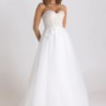 A woman stands against a plain white backdrop wearing the HADLEY PO926. The bodice is intricately detailed with lace and features a sweetheart neckline. The skirt is full with layers of tulle, adorned with floral appliqués at the waist, making it a perfect choice for any bride. Angels Formal Wear