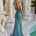 A woman stands beside an ornate pool, wearing a flowing, strapless, emerald green gown. Her back is to the camera, and her long, wavy hair cascades down her back. Classical statues and elegant columns decorate the surroundings with Alocasia PO24139 enhancing the luxurious atmosphere. Angels Formal Wear