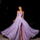 A woman wearing the flowing, sparkly STARLIGHT NC2029 lavender gown with a thigh-high slit poses against a dark background. Bathed in starlight, she stands confidently, holding out the sides of the dress to showcase its fabric and shimmer. She pairs the STARLIGHT NC2029 dress with high heels and has a serene expression. Angels Formal Wear