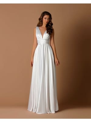 A woman stands against a plain brown background wearing the SKYLA NBM1013, a floor-length, sleeveless white gown featuring a deep V-neck and a cinched waist. Her long, wavy hair cascades down her shoulders as she maintains a neutral expression. Angels Formal Wear