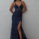 A woman in a sleeveless, deep V-neck KAIRI PO2460 evening gown in navy blue, embellished with sequins, stands against a light background. The dress features a thigh-high slit and she pairs it with white high-heeled sandals. Her hands rest on her hips and she has long, wavy hair. Angels Formal Wear