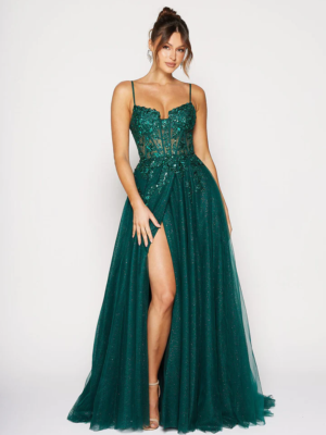 A woman stands confidently in the stunning NIARA PO2488 emerald-green gown, featuring spaghetti straps, intricate beadwork, and a high slit on one side. The dress flows elegantly to the floor, paired with nude heels. Her hair is styled in a chic updo with soft bangs. Angels Formal Wear