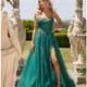 A woman in a teal, floor-length ARALIA PO24155 gown with a high slit stands in an outdoor setting, surrounded by classical statues. The gown features intricate embellishments and she is wearing long, dangling earrings and high-heeled sandals. Angels Formal Wear