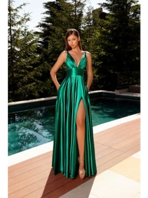 A woman in a sleeveless, emerald green SIENNA NC2052 satin gown with a deep V-neck and thigh-high slit stands on a wooden deck by a pool, surrounded by tall, green pine trees. Her long, straight hair cascades down as she elegantly poses in high-heeled sandals. The scene is reminiscent of Sienna’s serene charm. Angels Formal Wear