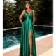 A woman in a sleeveless, emerald green SIENNA NC2052 satin gown with a deep V-neck and thigh-high slit stands on a wooden deck by a pool, surrounded by tall, green pine trees. Her long, straight hair cascades down as she elegantly poses in high-heeled sandals. The scene is reminiscent of Sienna’s serene charm. Angels Formal Wear