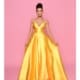 Against a pink backdrop, a woman elegantly poses in a striking floor-length BRENNA NP1 gown. The vibrant yellow dress features thin straps and a deep neckline. She holds the sides of the gown, slightly spreading it to display its fullness, while her hair is styled in an elegant updo. Angels Formal Wear