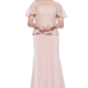 A woman stands wearing the FRANCESCA BEADED GOWN TL1159, a floor-length, short-sleeved evening dress in blush pink featuring a textured top and smooth skirt. With light-colored hair and a cheerful smile, she poses against a plain white background. Angels Formal Wear