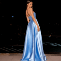 A woman stands on a tiled surface at night, draped in the elegant HAVANNA NC2030 gown—strapless, floor-length, and silky blue. She faces slightly away from the camera, allowing the graceful flow and sheen of her dress to be perfectly showcased. The dark background is softly illuminated by subtle hints of light that capture the charm of HAVANNA NC2030. Angels Formal Wear