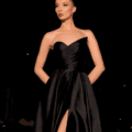 A woman is standing against a dark background, donning the stunning HAVANNA NC2030 strapless black gown that features a sophisticated thigh-high slit. Her hands rest comfortably in the dress's pockets as her hair is styled in a sleek and elegant updo. She gazes confidently into the distance, perfectly embodying the allure of HAVANNA's NC2030 collection. Angels Formal Wear