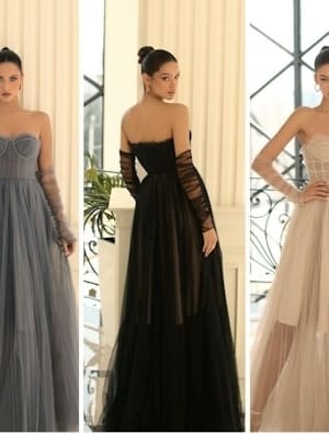 In a classical setting, three women strike a pose in elegant, strapless gowns with full tulle skirts and sheer gloves. Among them is the stunning IVY 1064 ensemble. The first woman wears a blue gown, the second dons a black one, and the third showcases a beige gown, all set against a backdrop of large windows and pillars. Angels Formal Wear