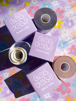 Displayed on a vibrant, floral background are five rolls of "GAL PALS TAPE." This collection features tapes in black, clear, and beige, each one nestled in its own box. Angels Formal Wear