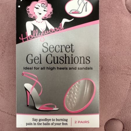 The packaging for HOLLYWOOD - GEL CUSHIONS, ideal for high heels and sandals, features a stylish pink shoe illustration. With text assuring relief from foot pain, these gel cushions are available in two pairs and are beautifully set against a pink textured background. Angels Formal Wear