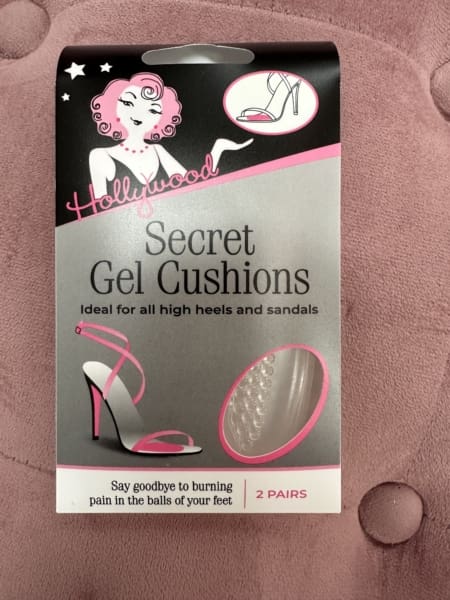 The packaging for HOLLYWOOD - GEL CUSHIONS, ideal for high heels and sandals, features a stylish pink shoe illustration. With text assuring relief from foot pain, these gel cushions are available in two pairs and are beautifully set against a pink textured background. Angels Formal Wear